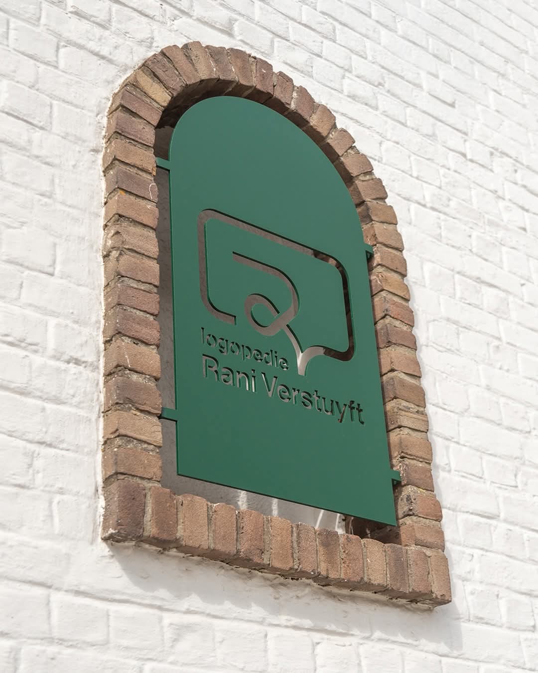 Groen naambord van Logopedie Rani Verstuyft in een bakstenen nis aan de gevel